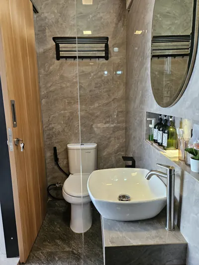Kamar mandi dengan wastafel bulat, cermin oval, shower, pemanas air, dan dinding bermotif marmer
